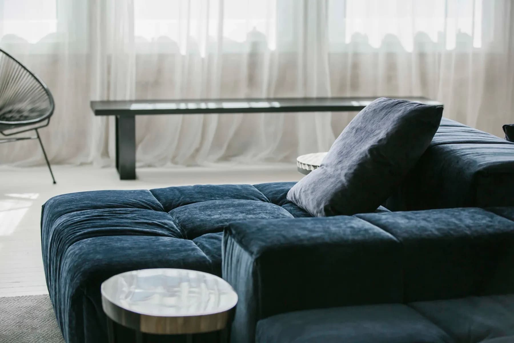 A navy velvet sofa and a wire lounge chair in front of long sheer curtains