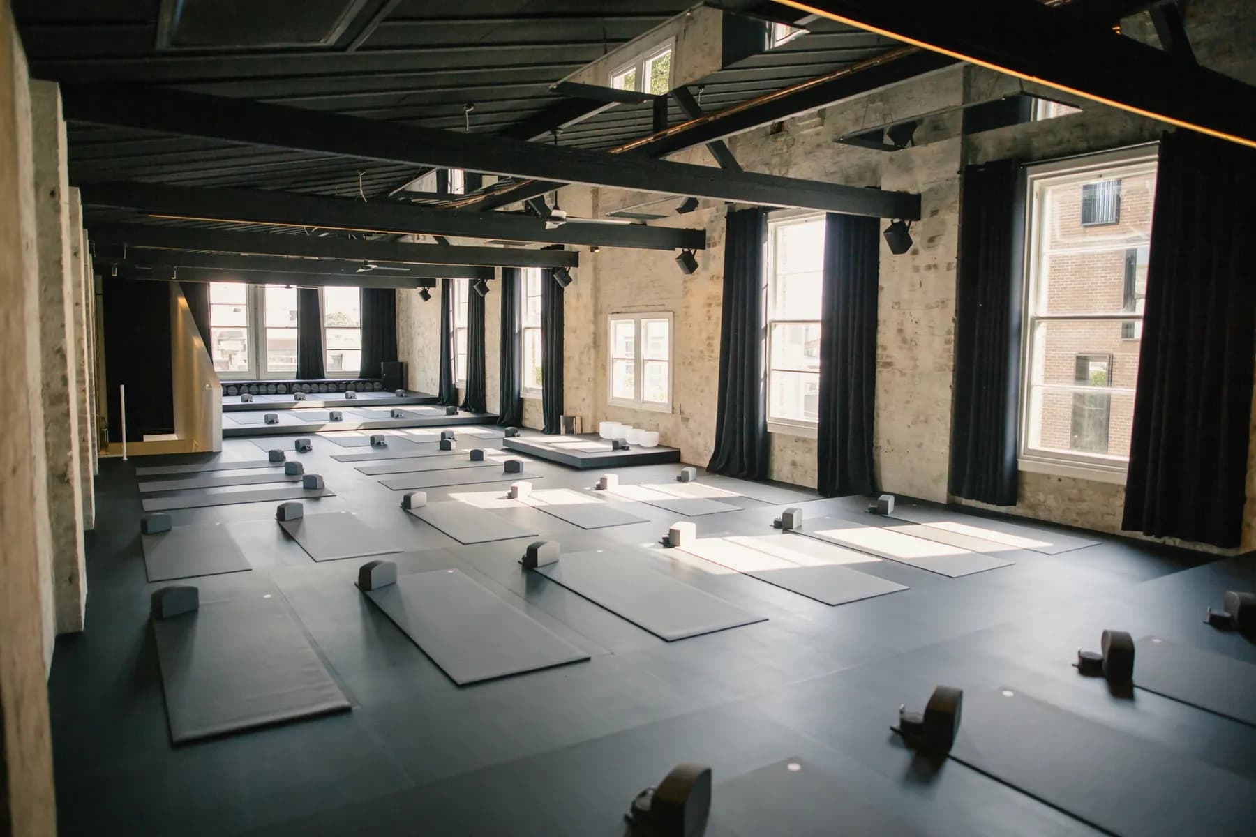 The practice room at Still Studio, with rows of mats under dark beams and tall windows
