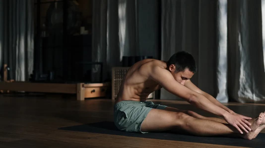 A person stretching forward on a yoga mat in a softly lit studio